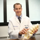 Dr. William Cobb Holding a Lumbar Spine Model, pointing at one of the vertebrae.